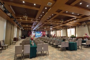 Un salón de conferencias con filas de sillas, un escenario con un cartel y un ventanal grande.