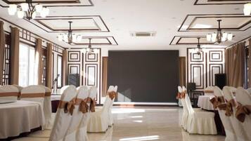 A banquet hall with rows of tables and chairs, a large screen, and chandeliers.