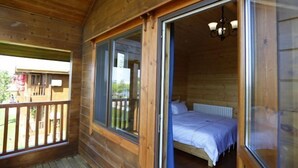 Una cabaña de madera con balcón, una cama con ropa blanca y una ventana con vistas al exterior.