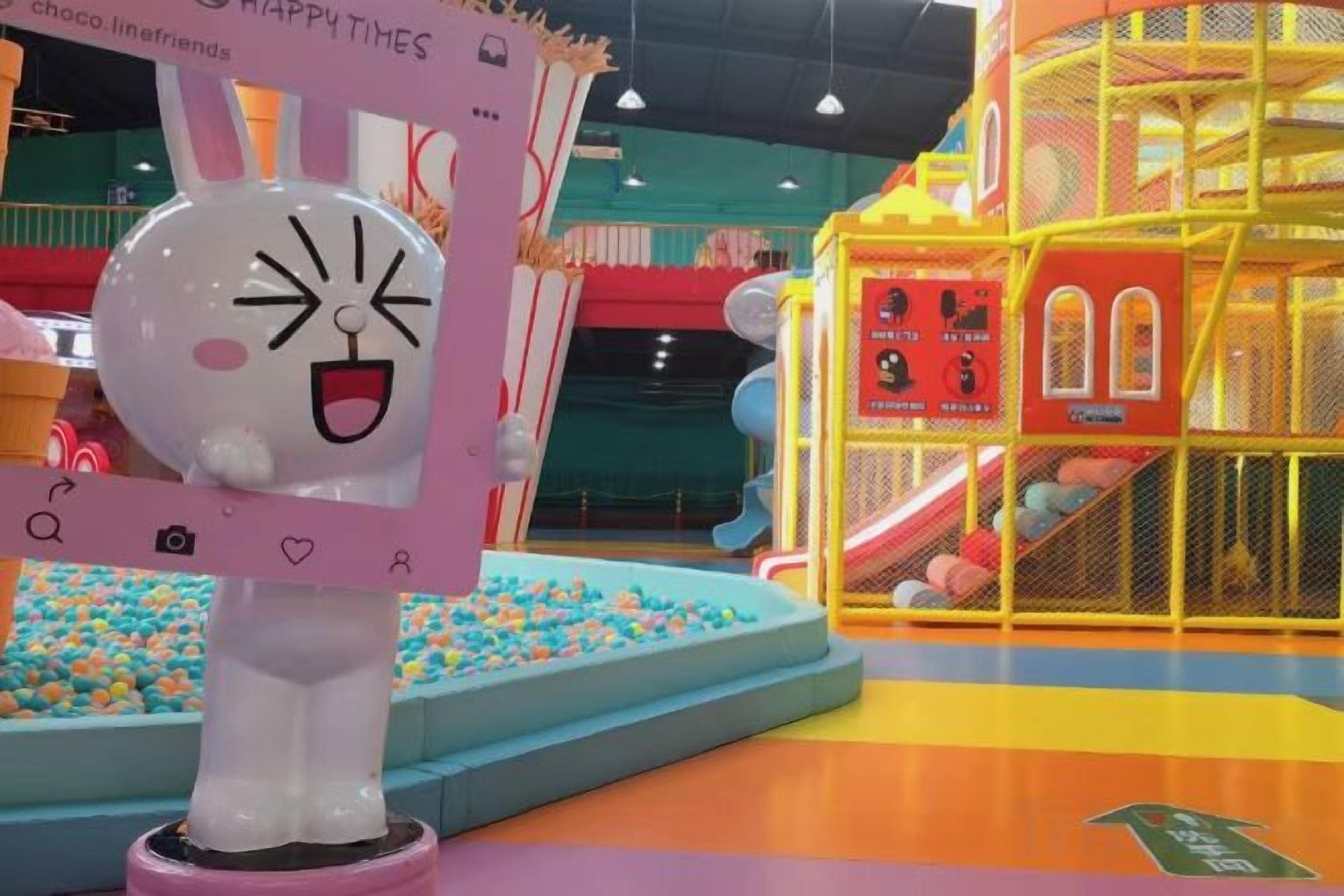 Een kinderspeelruimte met een bällebad, glijbanen en een grote witte en roze speelconstructie.