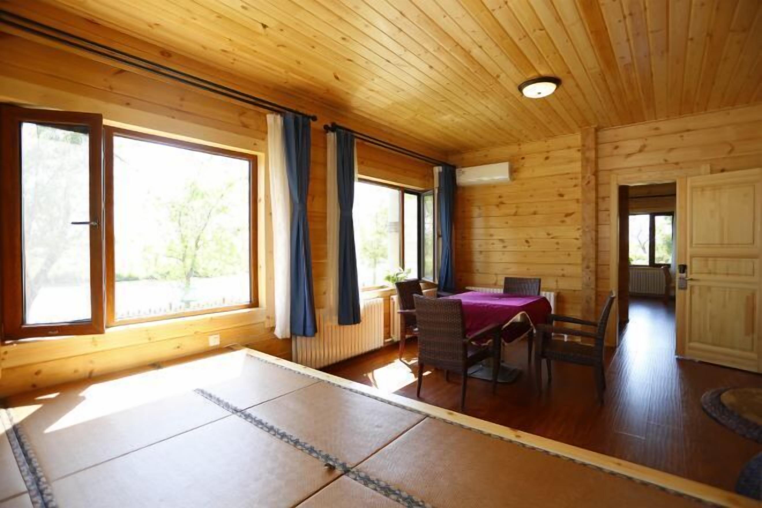 A wooden cabin with a dining area, large windows, and a view of greenery outside.