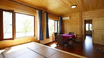 A wooden cabin with a dining area, large windows, and a view of greenery outside.