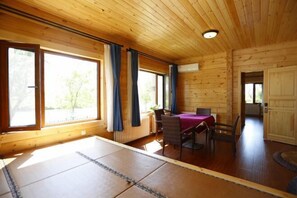A wooden cabin with a dining area, large windows, and a view of greenery outside.