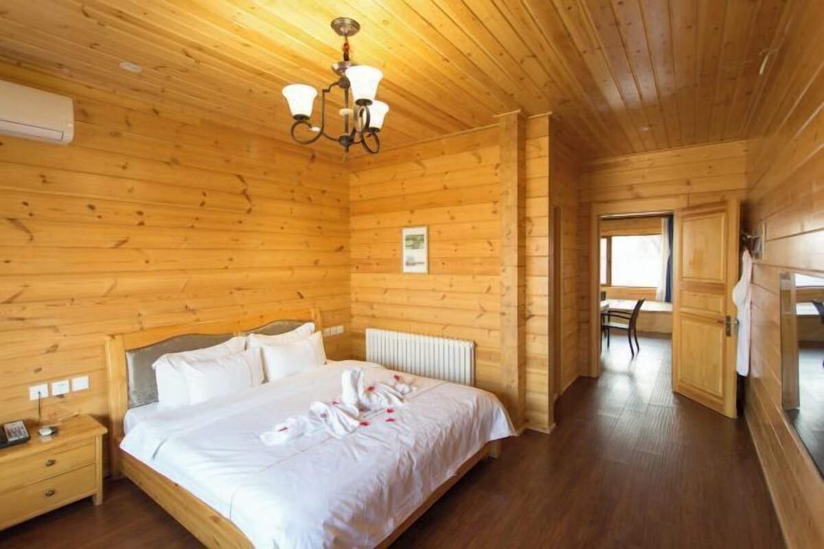 A wooden-paneled bedroom with a bed, a nightstand, a radiator, and a window.
