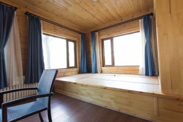 A room with wooden walls and floors, a bench along the windows, and a chair.