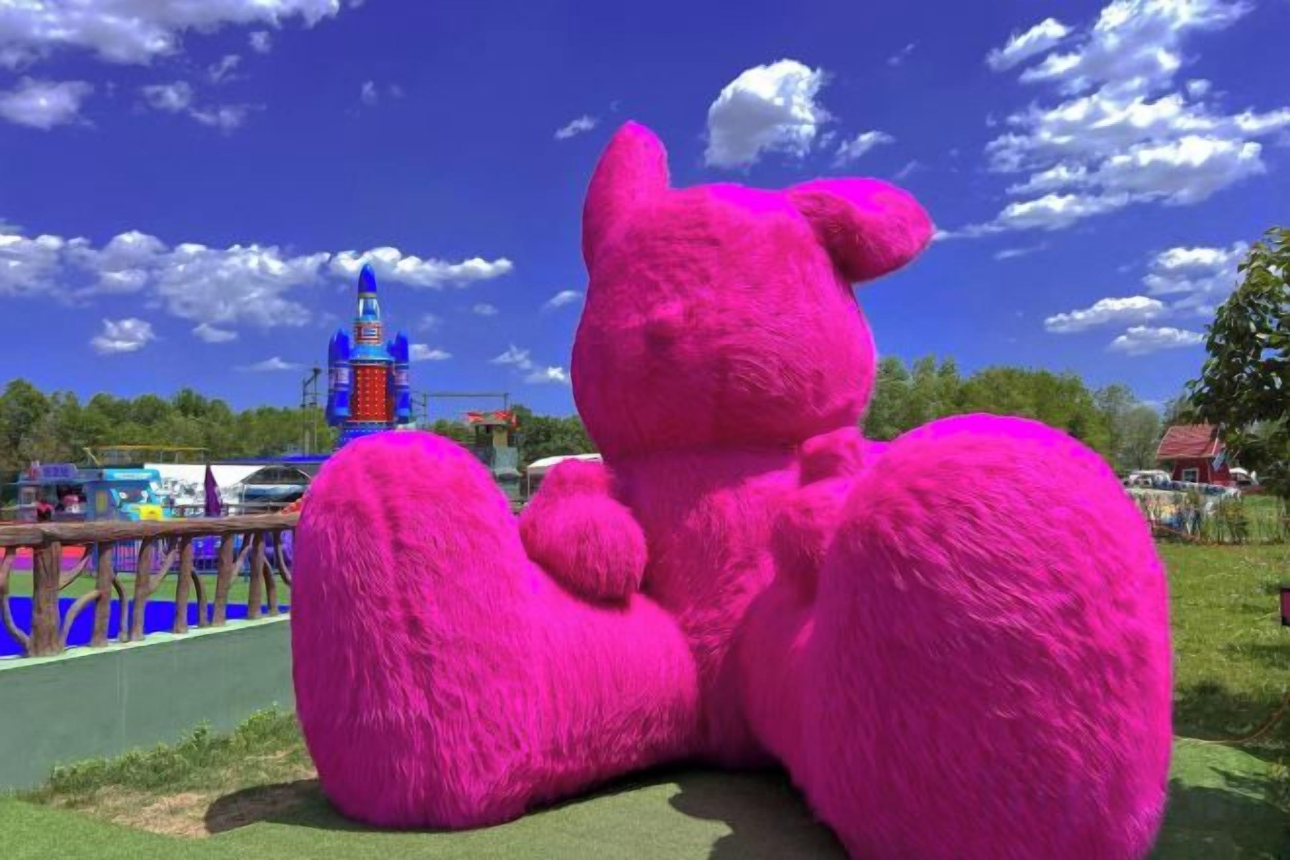 A large pink bear sculpture in an outdoor setting with a clear sky and a distant building.