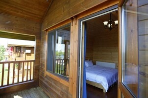 A wooden cabin with a balcony, a bed with white bedding, and a window with a view of the outside.