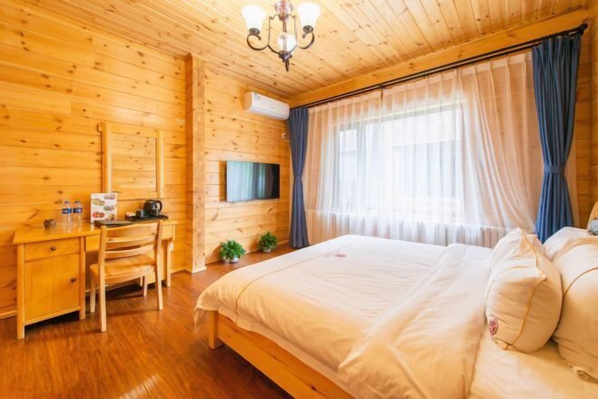 A wooden-paneled room with a bed, a desk, and a television.