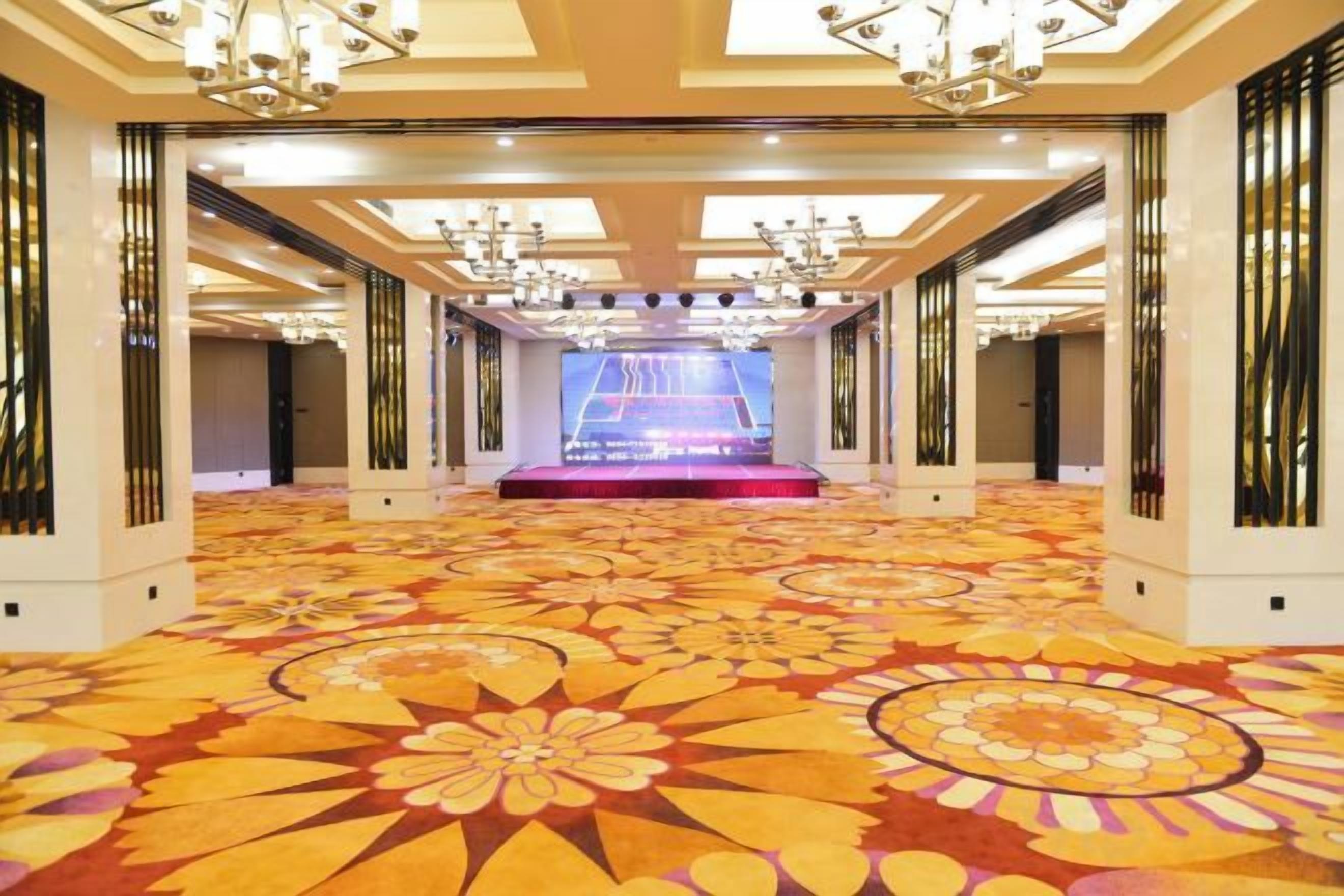 Un espacioso vestíbulo de hotel con un escenario central, candelabros ornamentados y una alfombra estampada.