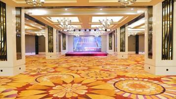 A spacious hotel lobby with a central stage, ornate chandeliers, and a patterned carpet.