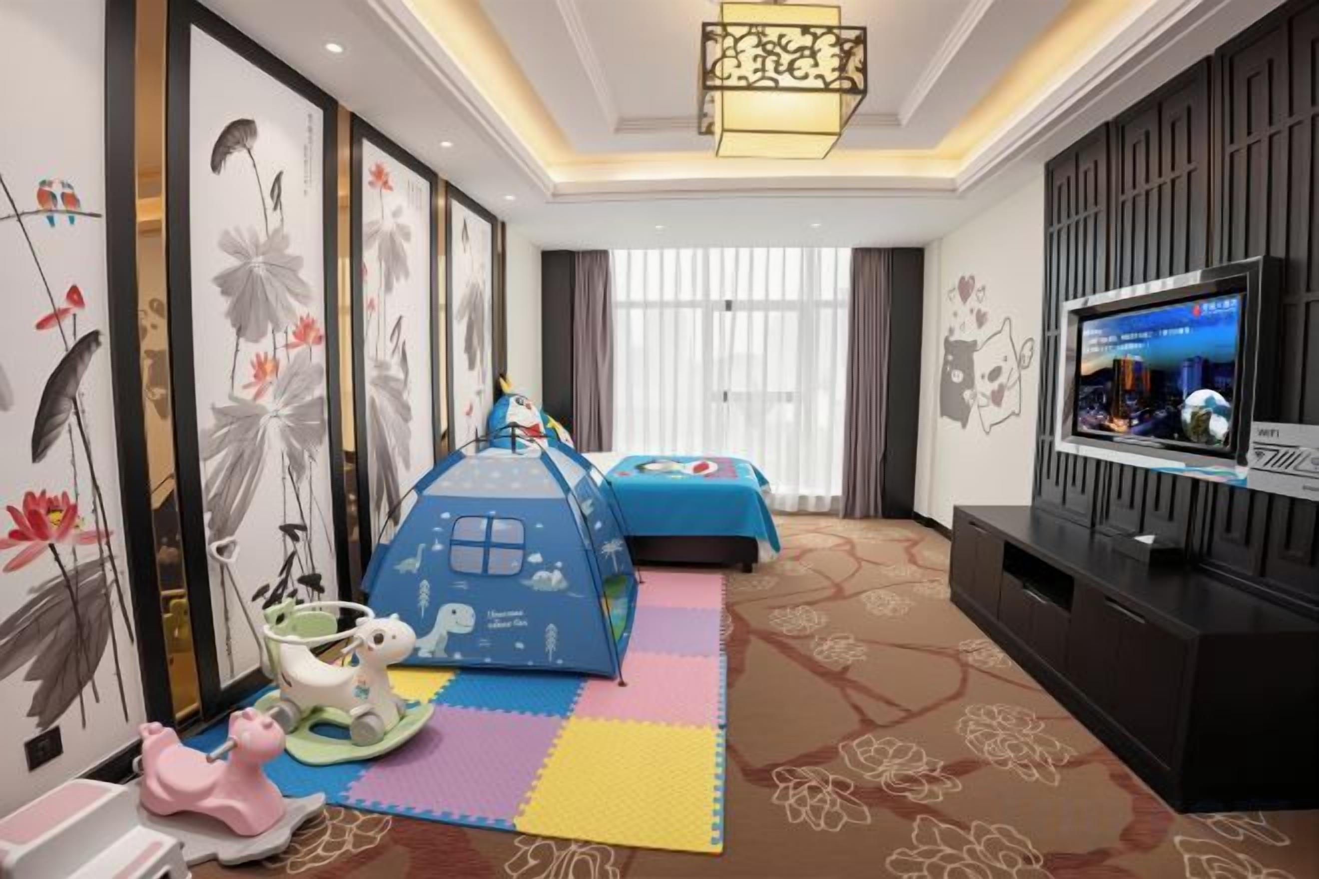 A hotel room with a TV, a bed, a play area, and artwork on the walls.