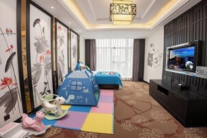 Una habitación de hotel con televisión, cama, zona de juegos y obras de arte en las paredes.