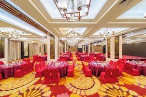 Un salón de banquetes con mesas redondas, sillas rojas y una alfombra estampada.