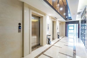 A hotel corridor with elevators, a trash bin, and a glass door leading to a room. - CHUXI GRAND HOTEL (Tongren)