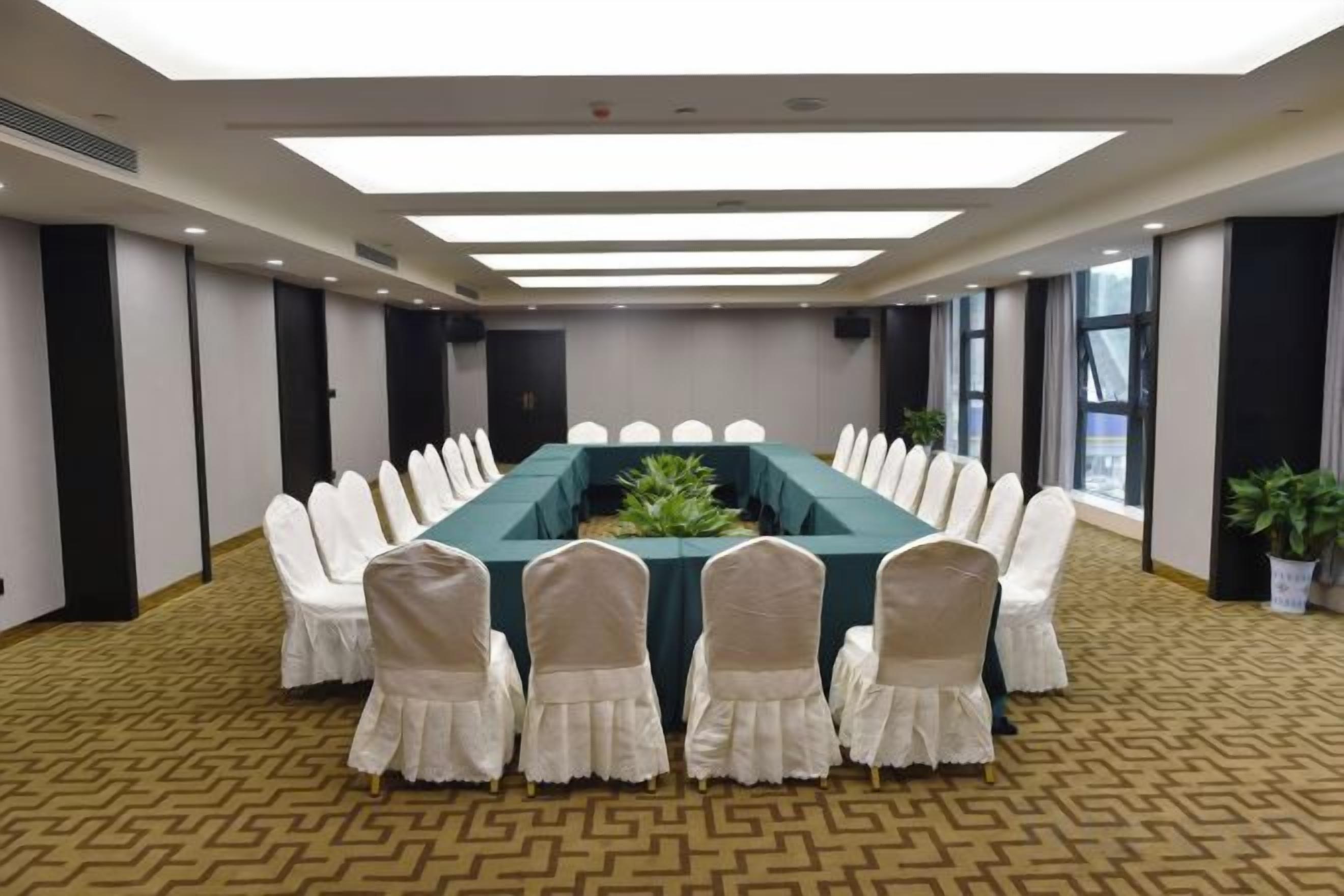 A conference room with a long table, white chairs, and a patterned carpet.