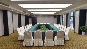 Sala de conferências com uma mesa comprida, cadeiras brancas e carpete estampado.