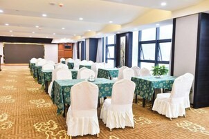 Un salón de conferencias con filas de mesas y sillas, suelo alfombrado y ventanas amplias.