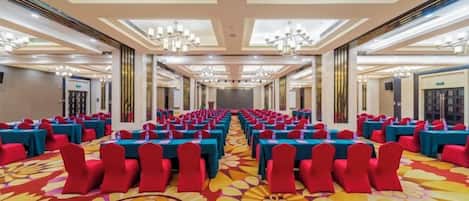 Un salón de conferencias con mesas y sillas dispuestas en filas, ventanas amplias y candelabros.