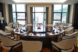 A conference room with a round table, chairs, and a view of a cityscape through large windows. - CHUXI GRAND HOTEL (Tongren)