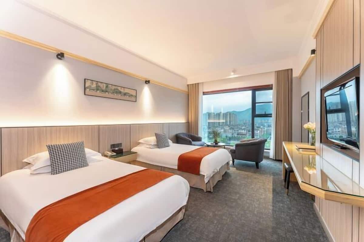 Quarto de hotel com duas camas, uma escrivaninha, uma cadeira, televisão e vista para a cidade.
