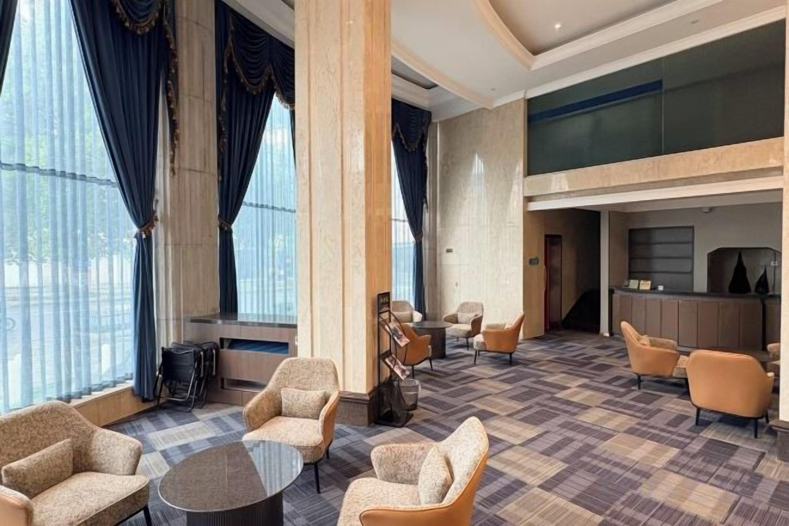 A hotel lobby with a check-in desk, seating area, and large windows.
