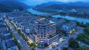 A multi-story hotel with a prominent curved facade, located near a river with a bridge in the background. - Oukai'er Hotel (Tonglu)