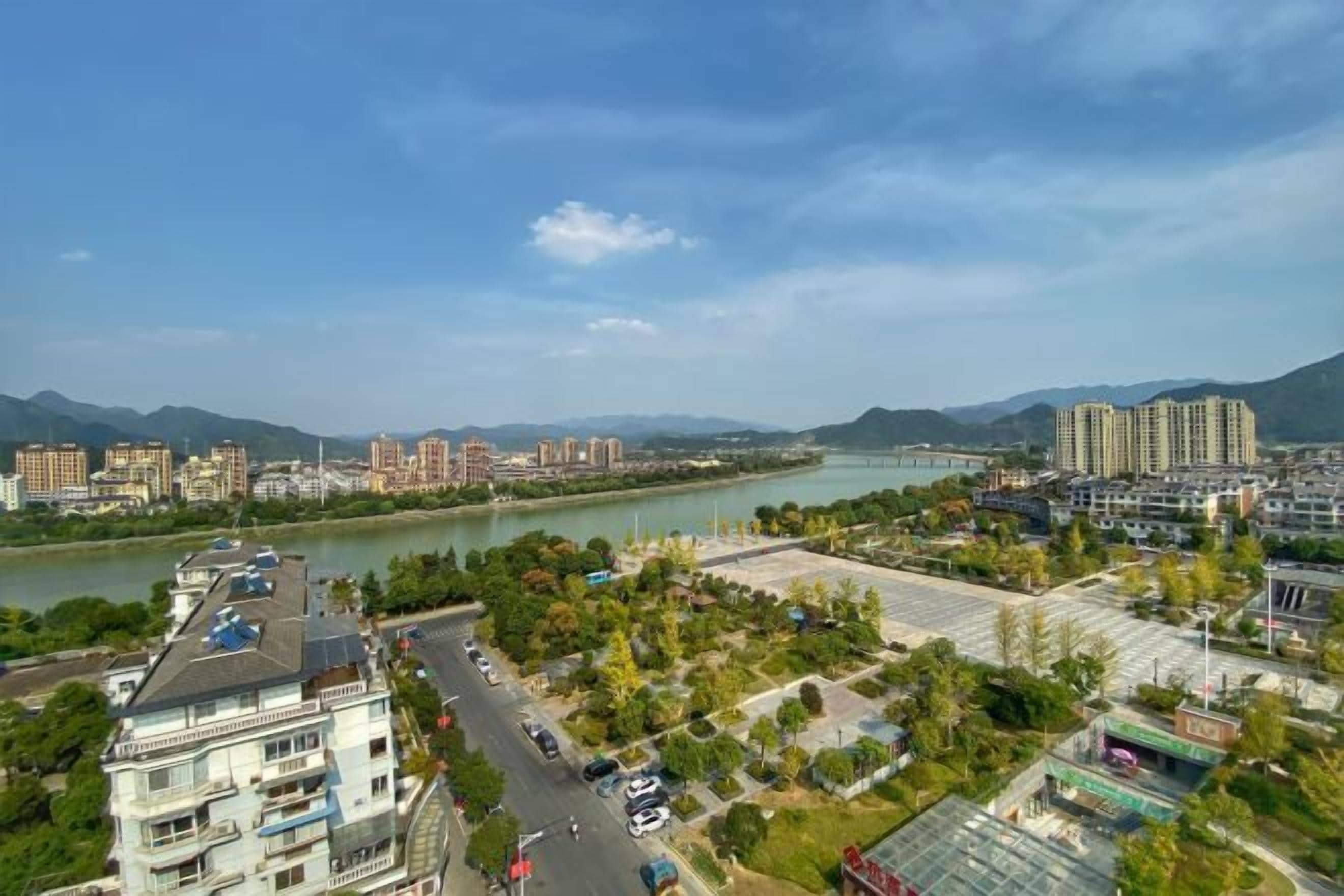 A river with buildings on the opposite bank, a bridge, and a mountainous backdrop.