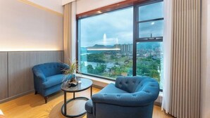 A modern living room with a large window offering a city view, two blue sofas, and a small round table with a plant. - Oukai'er Hotel (Tonglu)