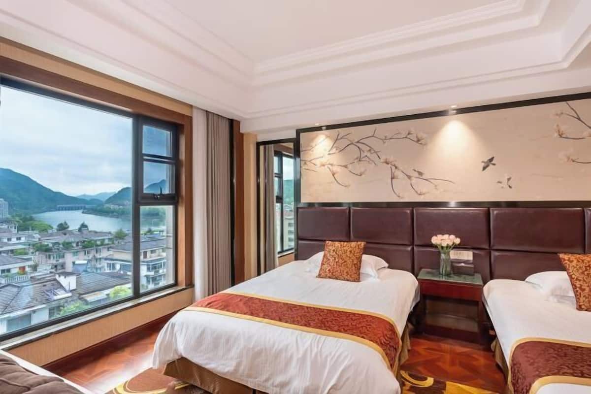 Quarto de hotel com duas camas, uma janela grande com vista para uma cidade e montanhas, e um objeto decorativo na parede.