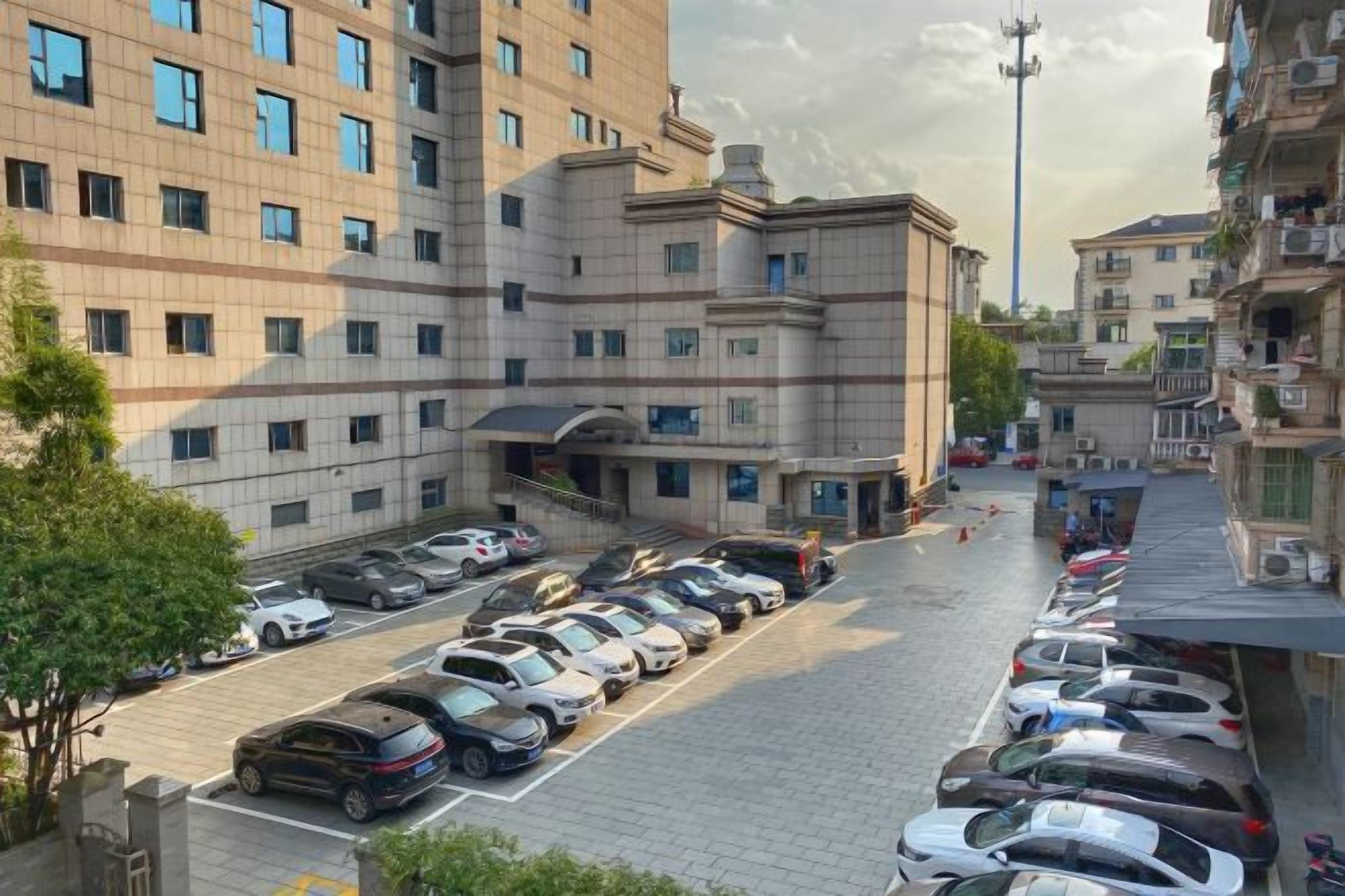 A multi-story hotel with a parking lot filled with cars, a central entrance, and a clear sky.