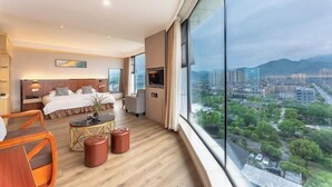 A modern hotel room with a large window, a bed, a desk, and a view of the cityscape. - Oukai'er Hotel (Tonglu)