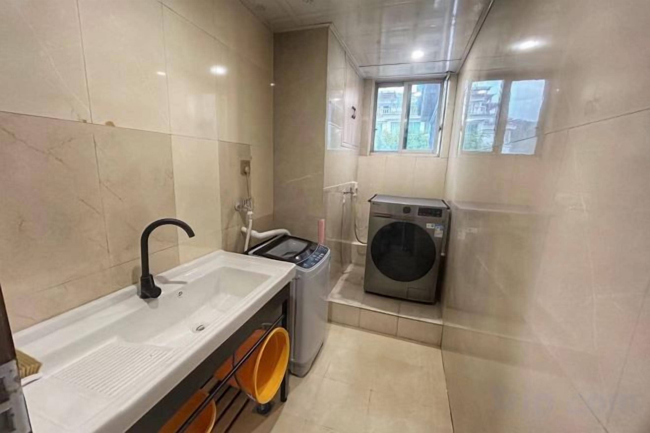 A compact bathroom with a sink, a washing machine, and a window.