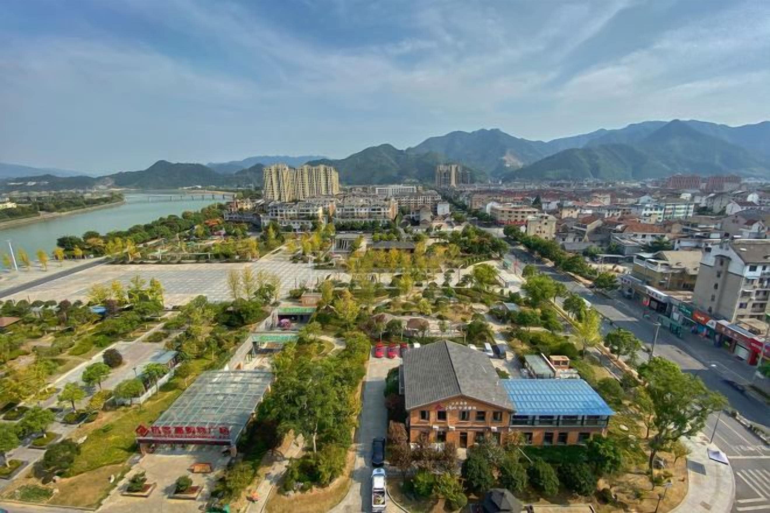 An aerial view of a cityscape with buildings, a river, and mountains in the background.