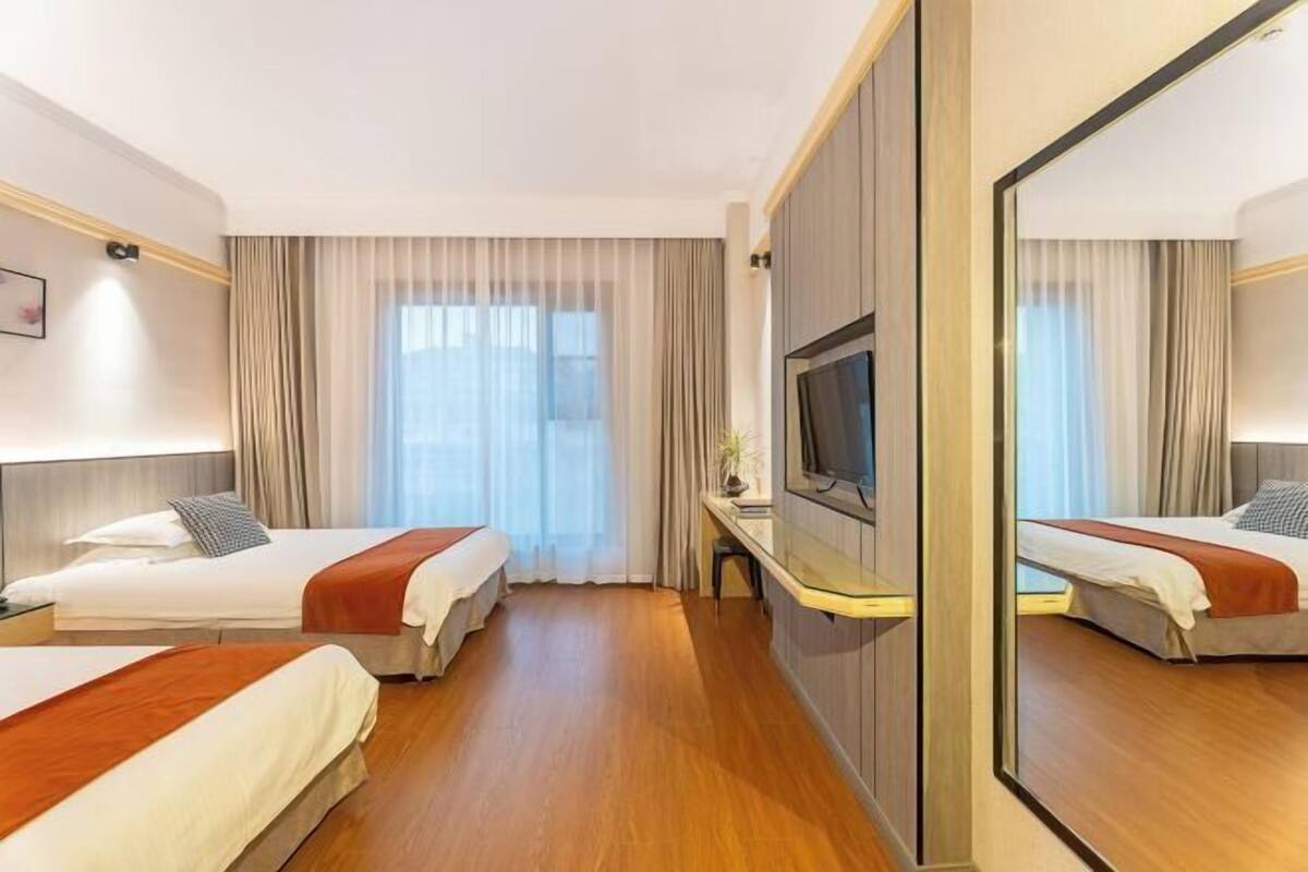 Quarto de hotel com duas camas, televisão, escrivaninha e um espelho grande.