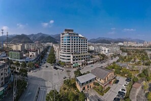 A multi-story hotel with a modern design, surrounded by a cityscape and mountains in the background. - Oukai'er Hotel (Tonglu)
