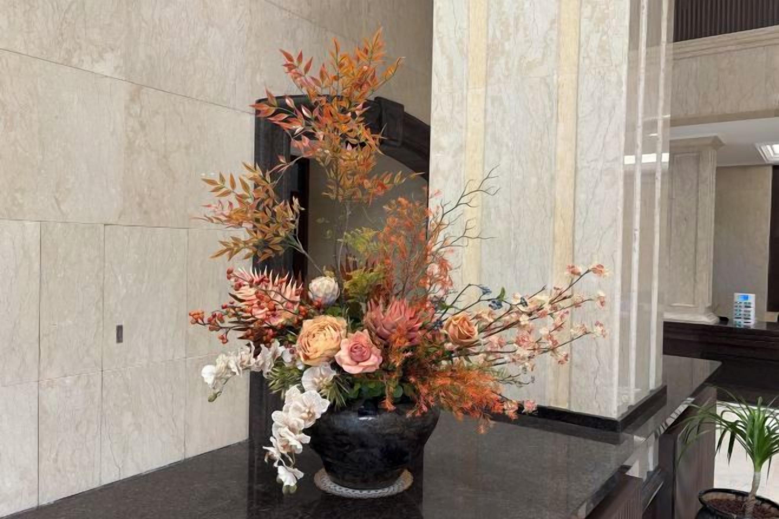 Un arrangement floral sur un comptoir en marbre dans un hall d’entrée, avec un miroir et une plante en pot.
