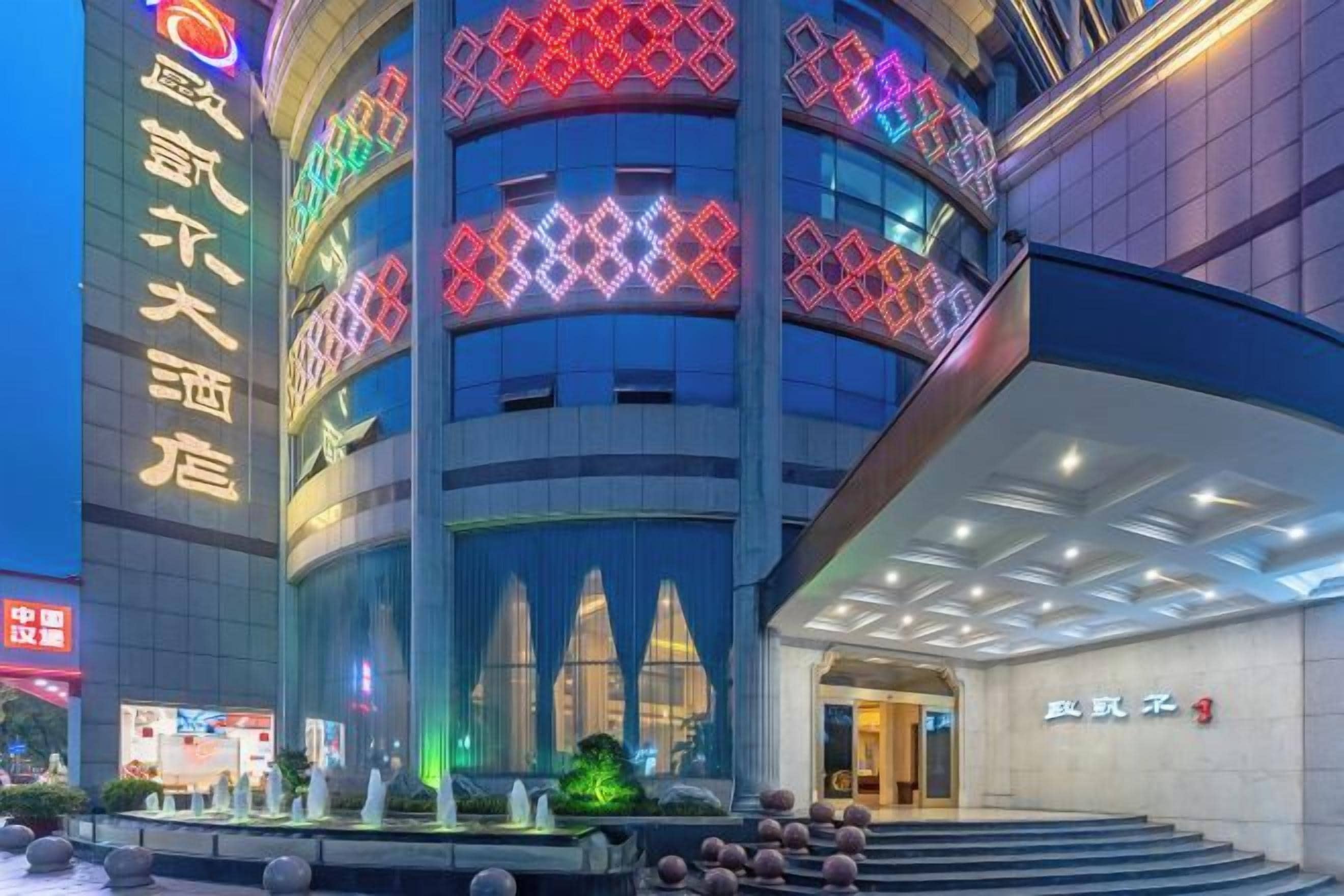 Un hotel de varios pisos con diseño moderno, que cuenta con una entrada destacada con fachada de vidrio y señalización iluminada.