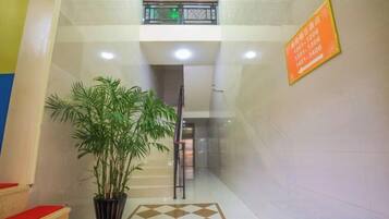 Een hotellobby met een trap, een potplant en een geruit vloerkleed.