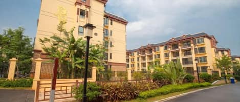 Un hotel de varios pisos con un patio central, entrada protegida por un portón y un jardín cuidado.