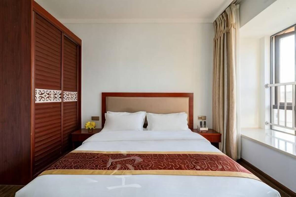 Een hotelkamer met een groot bed, een houten kast, een nachtkastje met een lamp en een raam met gordijnen.