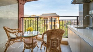 Een balkon met rieten meubilair, een ronde tafel en uitzicht op gebouwen.