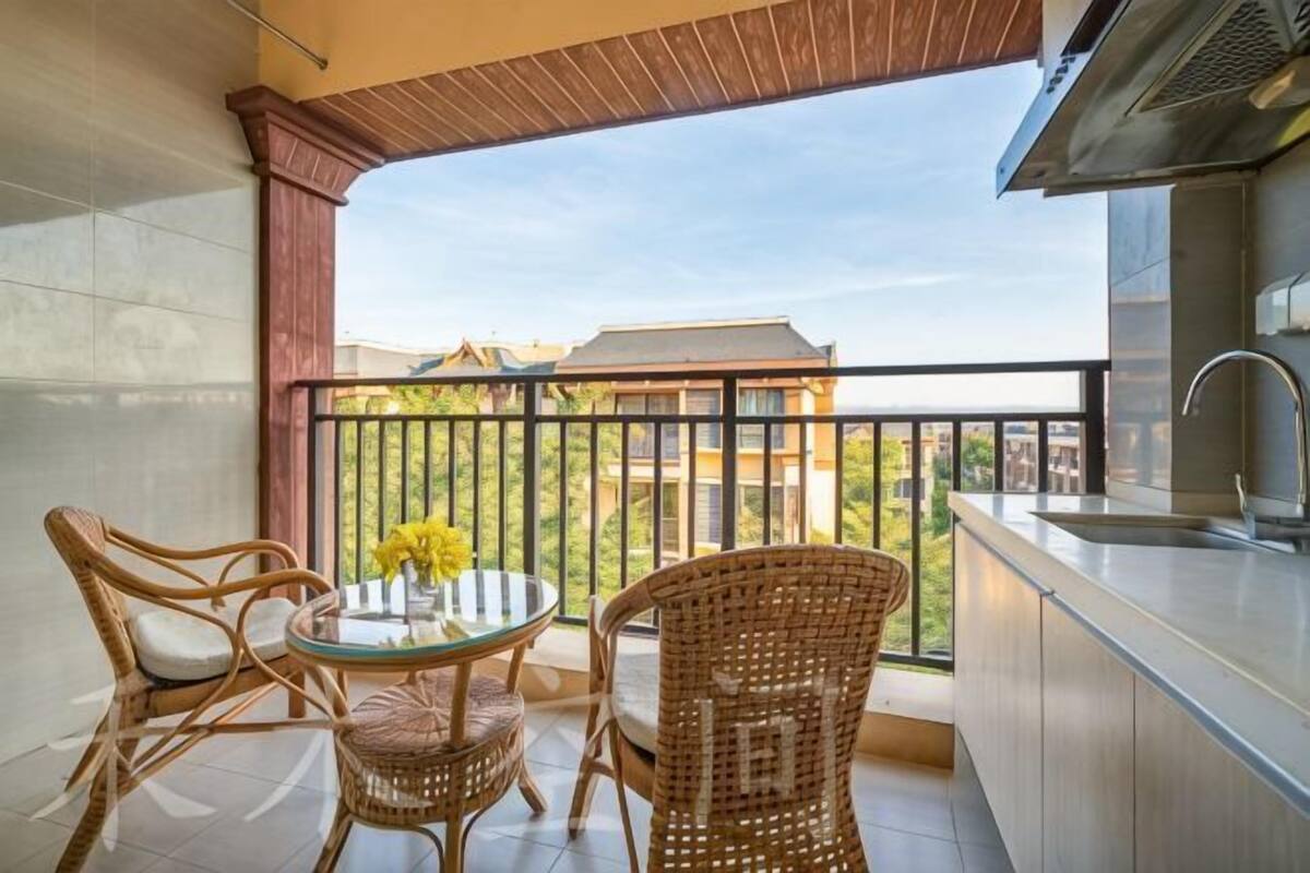 Een balkon met rieten meubilair, een ronde tafel en uitzicht op gebouwen.