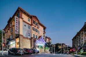A multi-story hotel with a prominent sign, parked cars, and a well-lit street. - Beautful holiday lnn (Jinghong)