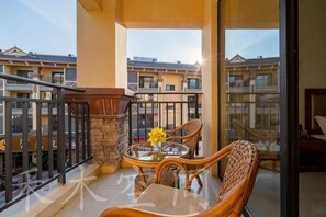 Un balcon doté de meubles en osier, d’une table en verre et offrant une vue sur d’autres immeubles.