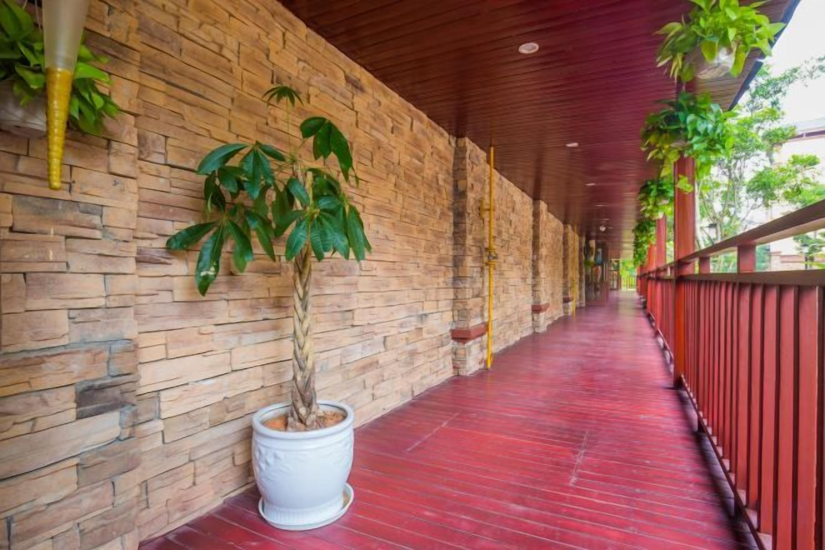 A corridor with a brick wall, a potted plant, and a red floor.