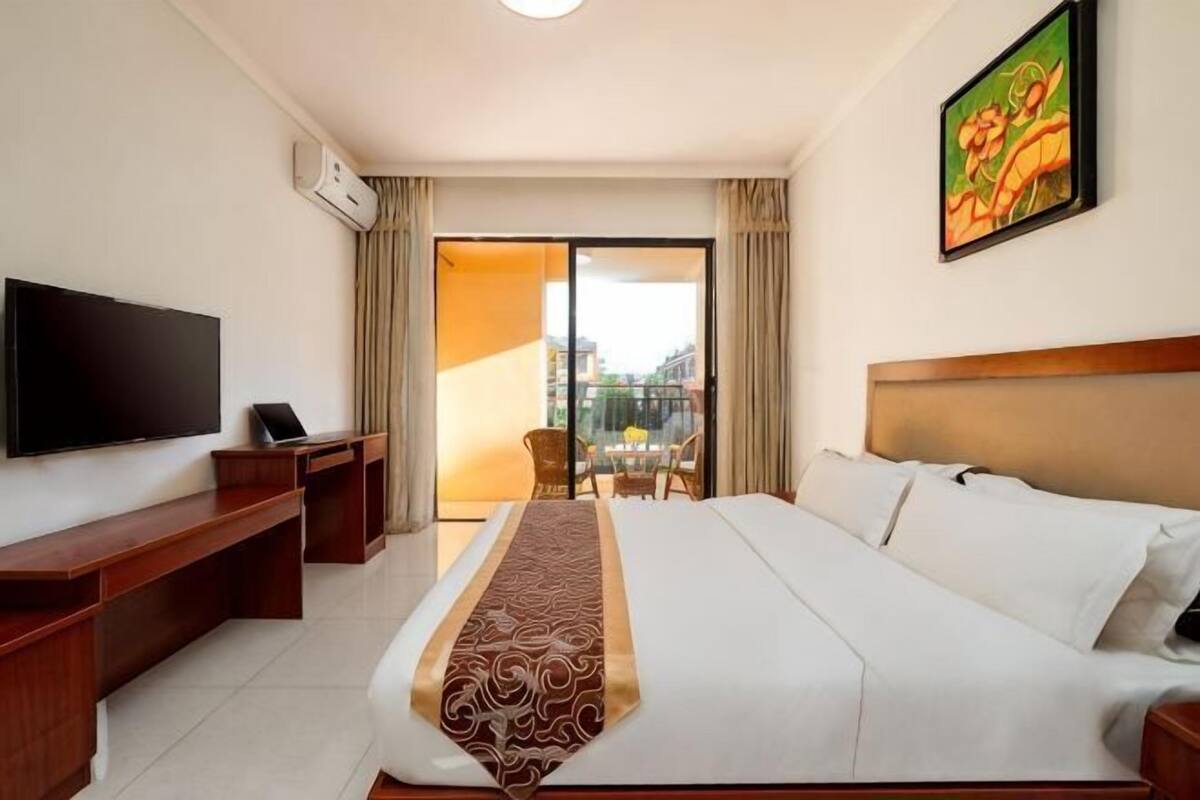 Een hotelkamer met een bed, een bureau, een televisie en een balkon met uitzicht.
