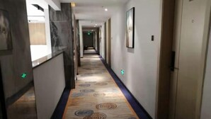 A hotel corridor with a patterned carpet, a reception desk, and a door at the end.