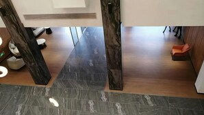 A modern hotel lobby with dark marble flooring, wooden pillars, and a seating area with a single orange chair.