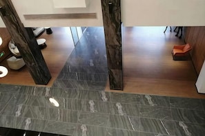 Un hall dâhĂŽtel moderne avec un sol en marbre foncĂ©, des piliers en bois et un espace dĂ©tente agrĂ©mentĂ© dâun seul fauteuil orange.