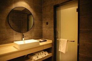 A modern bathroom with a white sink, a round mirror, and a towel hanging on a door. - Yicheng Hotel (Maoming China First Beach) (Maoming)